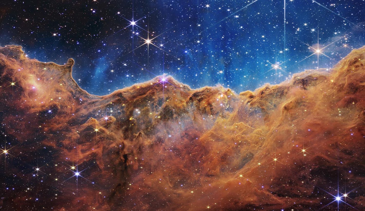Towering orange cliffs of gas under a deep blue sky full of bright stars